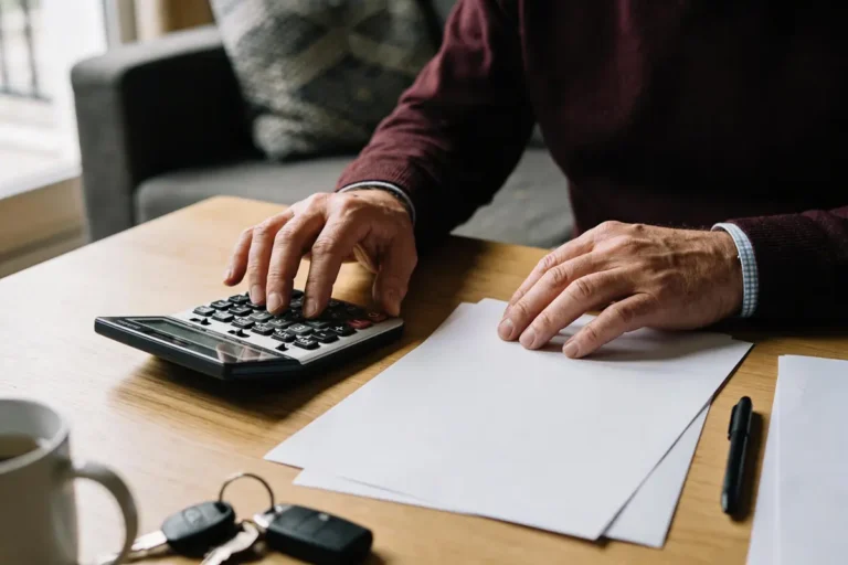 Personne utilisant une calculatrice avec des documents sur une table en bois, tasse et clés visibles.