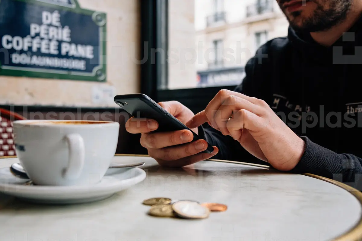 Homme utilisant un smartphone dans un café, tasse de café et pièces sur la table en marbre.