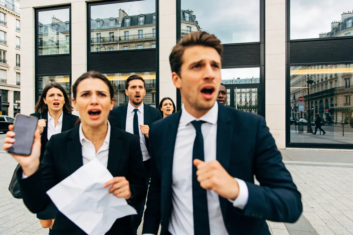 Groupe de personnes en costumes, expressions choquées, tenant téléphone et papier, devant bâtiment urbain.