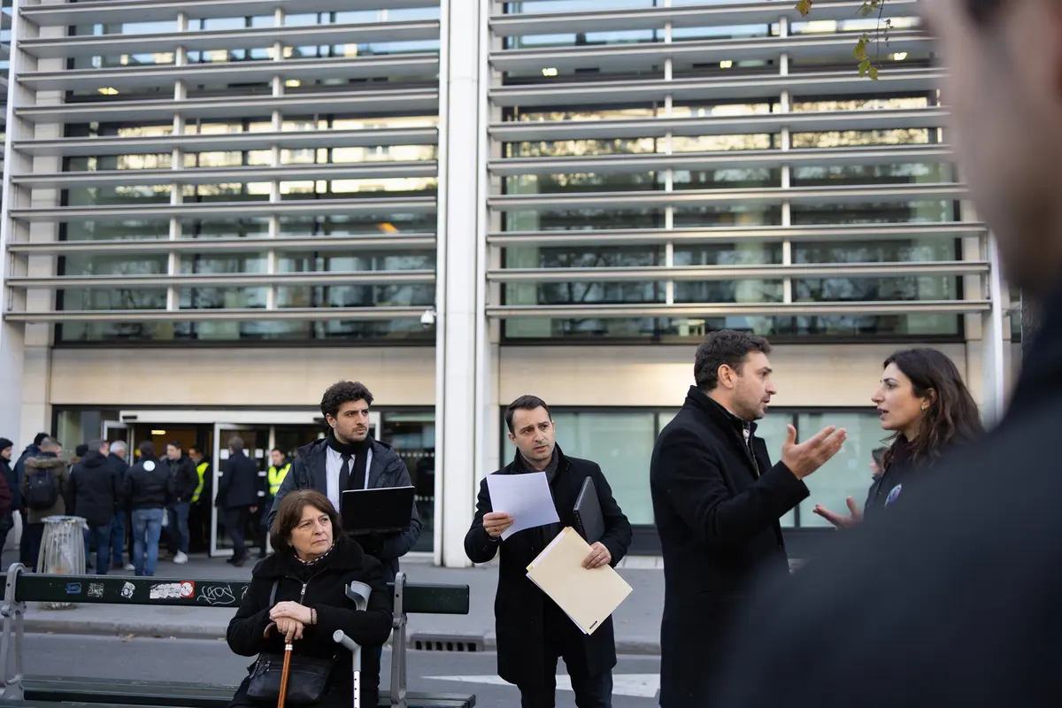 Groupe de personnes conversant devant un bâtiment moderne. Une femme est assise sur un banc.