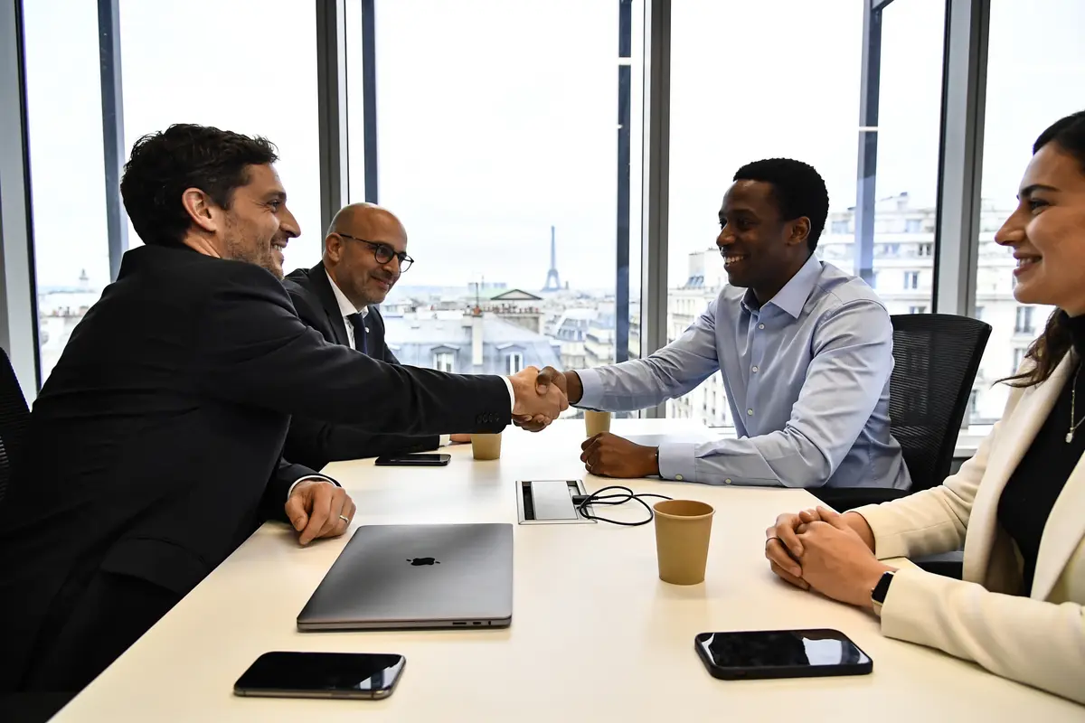 Quatre personnes en réunion, deux hommes se serrent la main dans un bureau avec vue sur la Tour Eiffel.