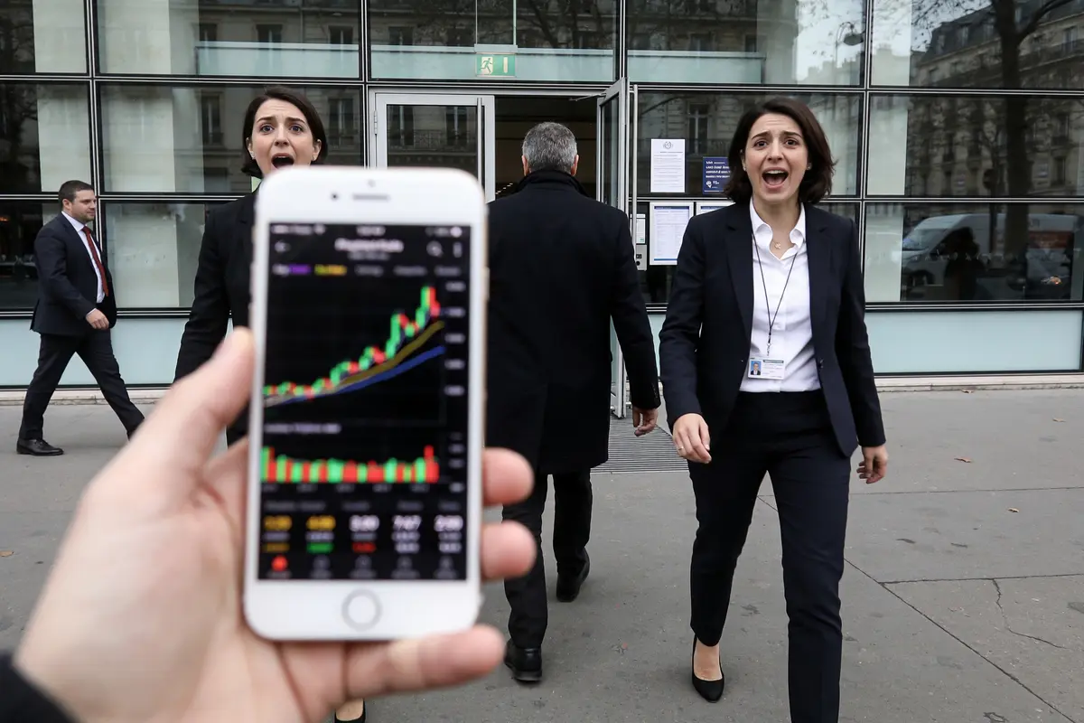Téléphone affichant graphique boursier, deux personnes surprises en costume devant un bâtiment moderne.