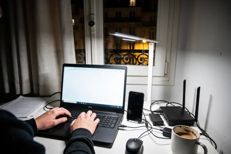 Personne tapant sur ordinateur portable près de fenêtre, smartphone, routeur et tasse de café sur le bureau.