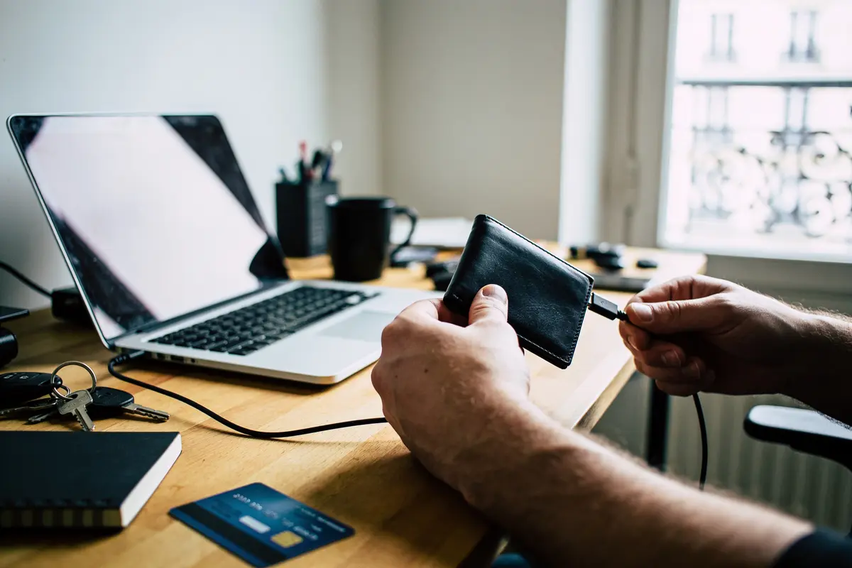 Une personne insère un câble dans un portefeuille digital près d'un ordinateur portable sur un bureau.