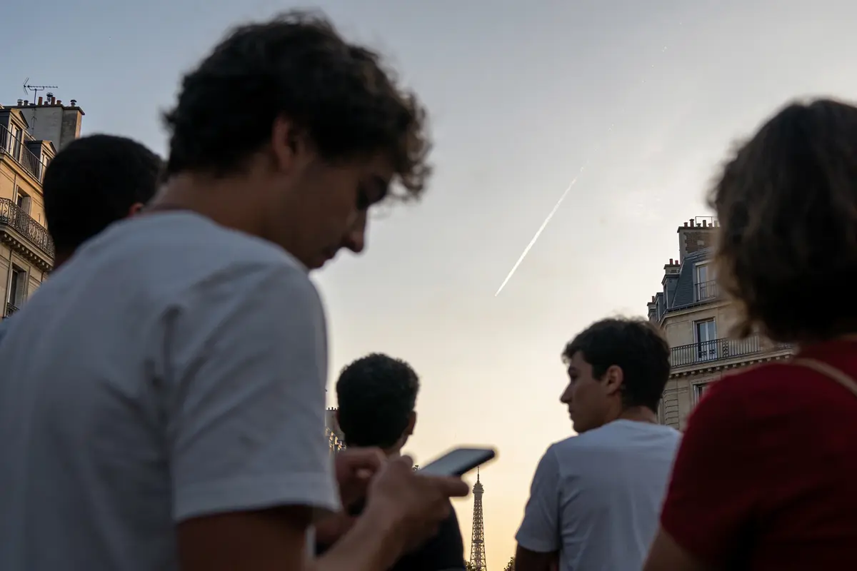 Des personnes regardant le ciel au crépuscule, avec la Tour Eiffel en arrière-plan.