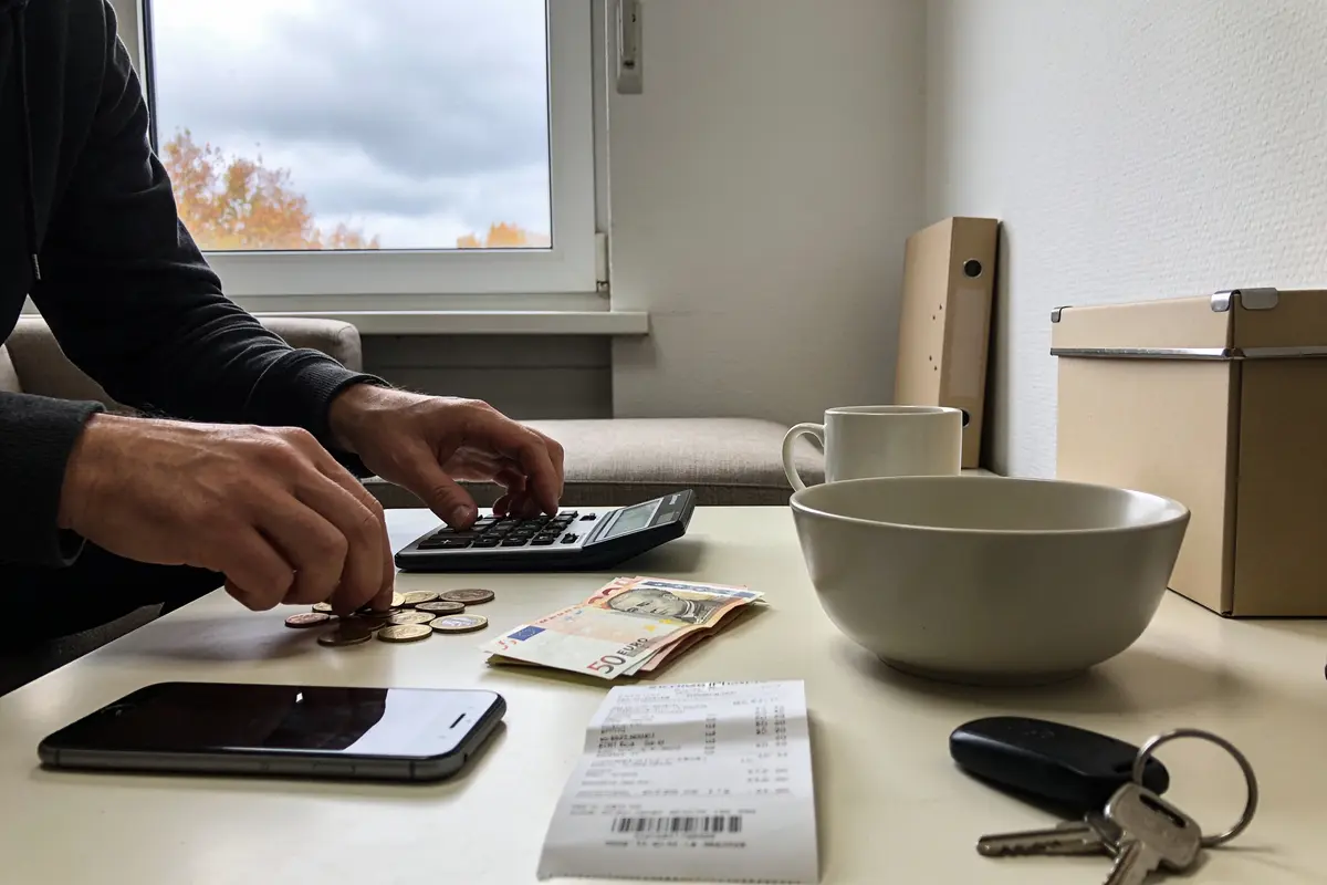 Une personne compte de l’argent avec une calculatrice sur une table, entourée d'objets divers.